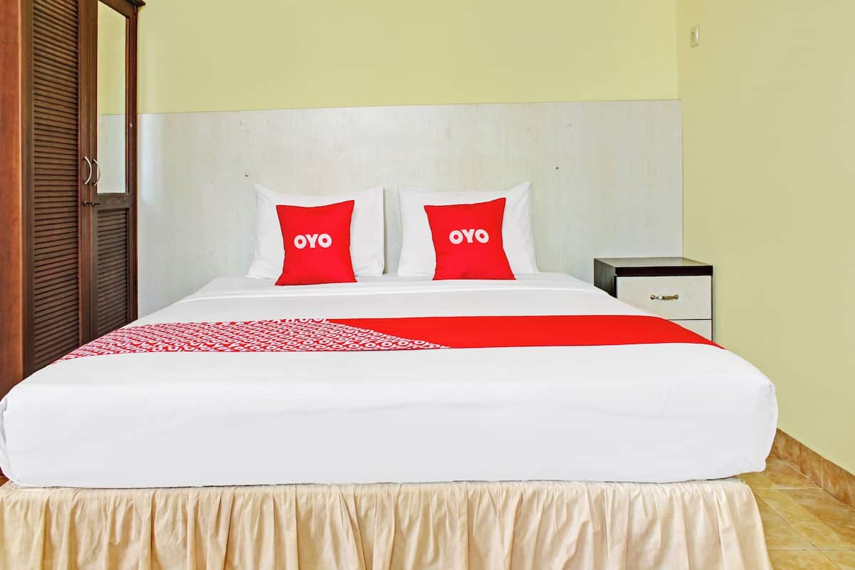 A hotel room with a bed, two pillows with the word "OYO" on them, a bedside table, and a wardrobe.