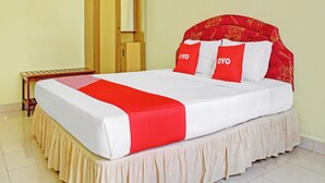 Un lit bien fait, recouvert d’une courtepointe rouge et blanche, avec deux oreillers rouges ornés du mot « OYO », et une armoire en bois dotée d’un miroir.