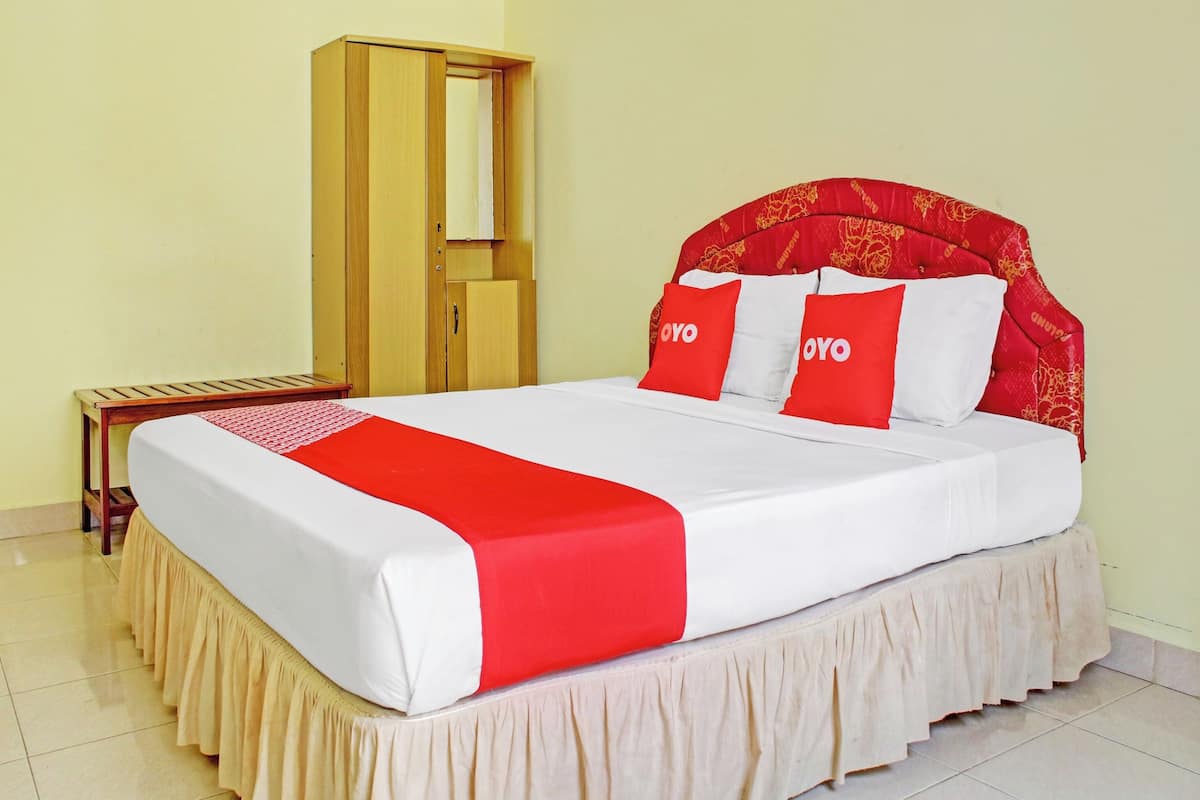 A neatly made bed with a red and white bedspread, two red pillows with the word "OYO" on them, and a wooden wardrobe with a mirror.