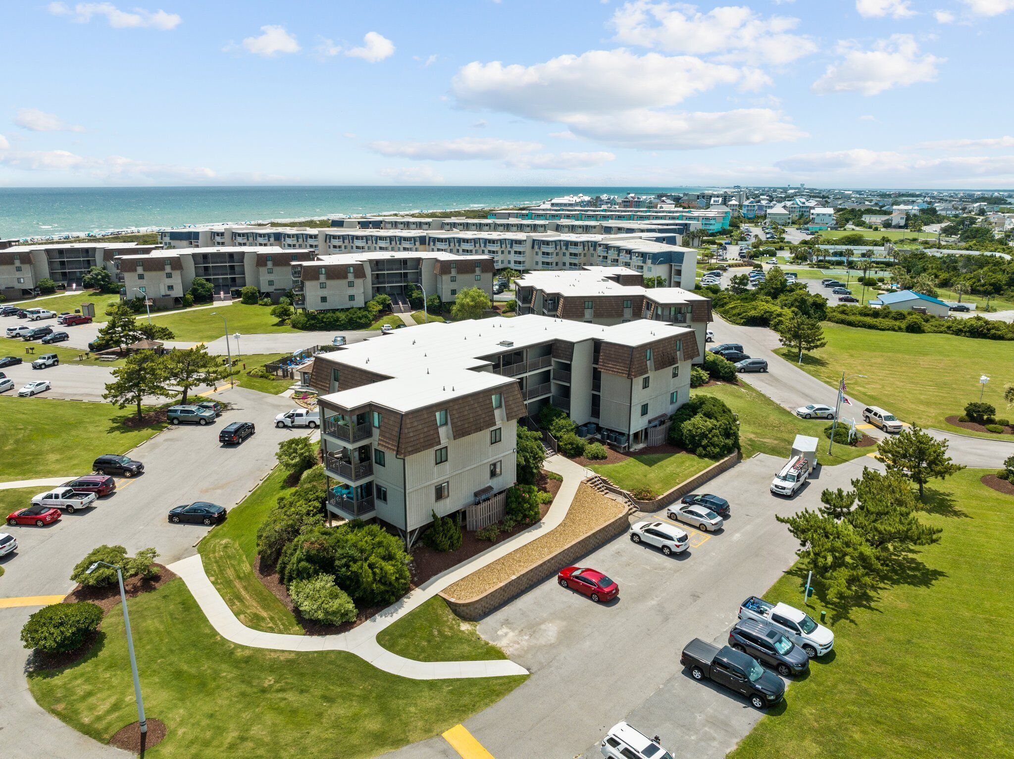 A multi-story residential building with a parking lot and a view of the ocean.