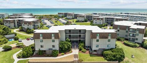 A residential complex with multiple apartment buildings, a parking lot, and a view of the ocean.