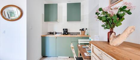 A compact kitchen with teal cabinets, a wooden dining table, and a rustic decor piece.
