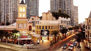 A hotel with a clock tower, surrounded by high-rise buildings and palm trees. - Chevron Renaissance Private room Lvl16 (Surfers Paradise)