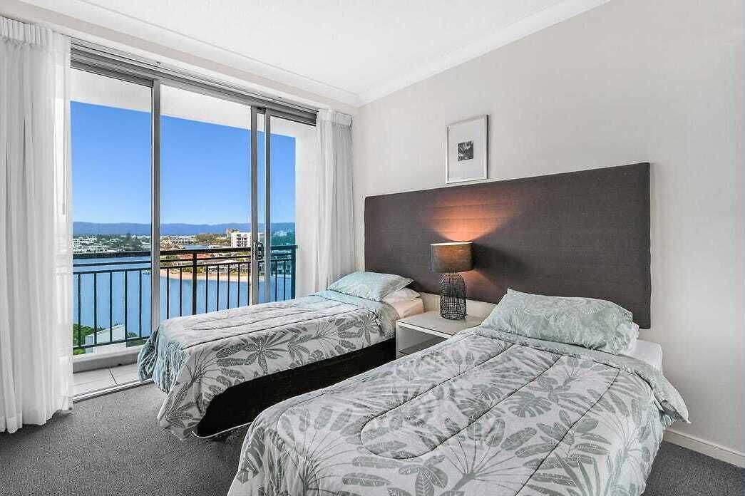 Une chambre d’hôtel avec deux lits, une grande fenêtre donnant sur la ville et une table de chevet avec une lampe.