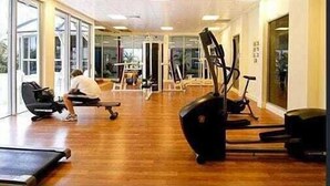 A gym with exercise equipment, a person using a treadmill, and large windows allowing natural light. - Chevron Renaissance Private room Lvl16 (Surfers Paradise)