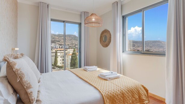 A hotel room with a large bed, a view of the city, and a hanging light fixture. - Barreiros Residence I (Funchal)