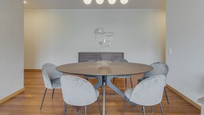 A modern dining area with a round table, grey upholstered chairs, a wooden cabinet, and a pendant light fixture. - Barreiros Residence I (Funchal)