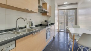 A modern kitchen with stainless steel appliances, a built-in oven, and a sink. There is a dining area with a white table and chairs. - Barreiros Residence I (Funchal)