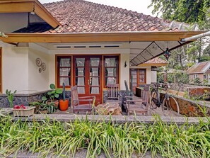 A house with a tiled roof, a porch with wooden furniture, and a garden area with plants and a cactus.