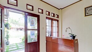 A reception area with a wooden reception desk, a sign reading "RECEPTIONIST," and a potted plant. - Collection O 90461 Graha Atmadja Syariah Guest House (Lembang)