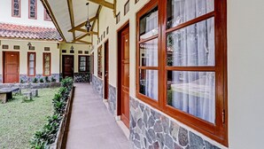 A corridor with stone walls, wooden doors, and windows with curtains. - Collection O 90461 Graha Atmadja Syariah Guest House (Lembang)