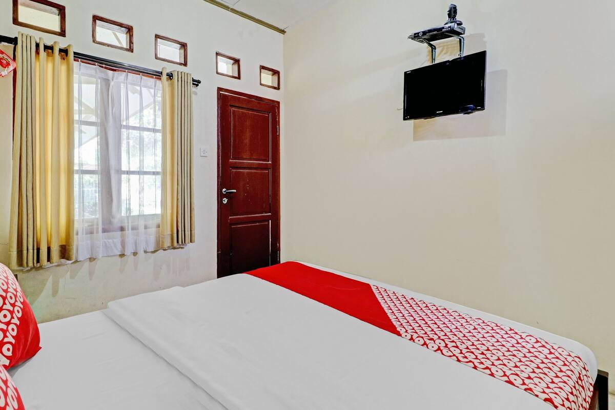 A hotel room with a bed, a window with curtains, a door, and a mounted TV.