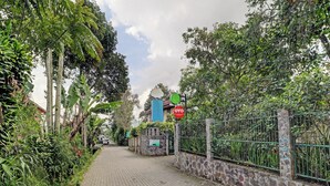 A paved pathway flanked by lush greenery and a stone wall with a metal fence. - Collection O 90461 Graha Atmadja Syariah Guest House (Lembang)
