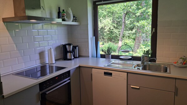 A modern kitchen with white tiles, a Siemens dishwasher, a coffee maker, and a window with a view of greenery.