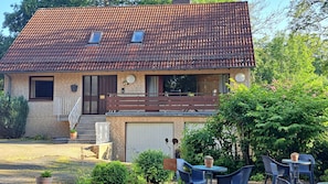 A two-story house with a tiled roof, a balcony, and a small garden area with outdoor seating.