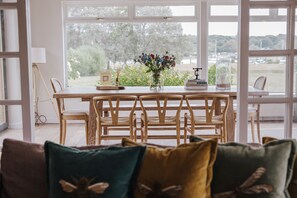 Un coin repas avec une table et des chaises en bois, un vase rempli de fleurs et une vue sur la verdure à l’extérieur.
