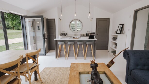 Een moderne keuken met een centraal eiland, barkrukken en een eethoek met houten stoelen.