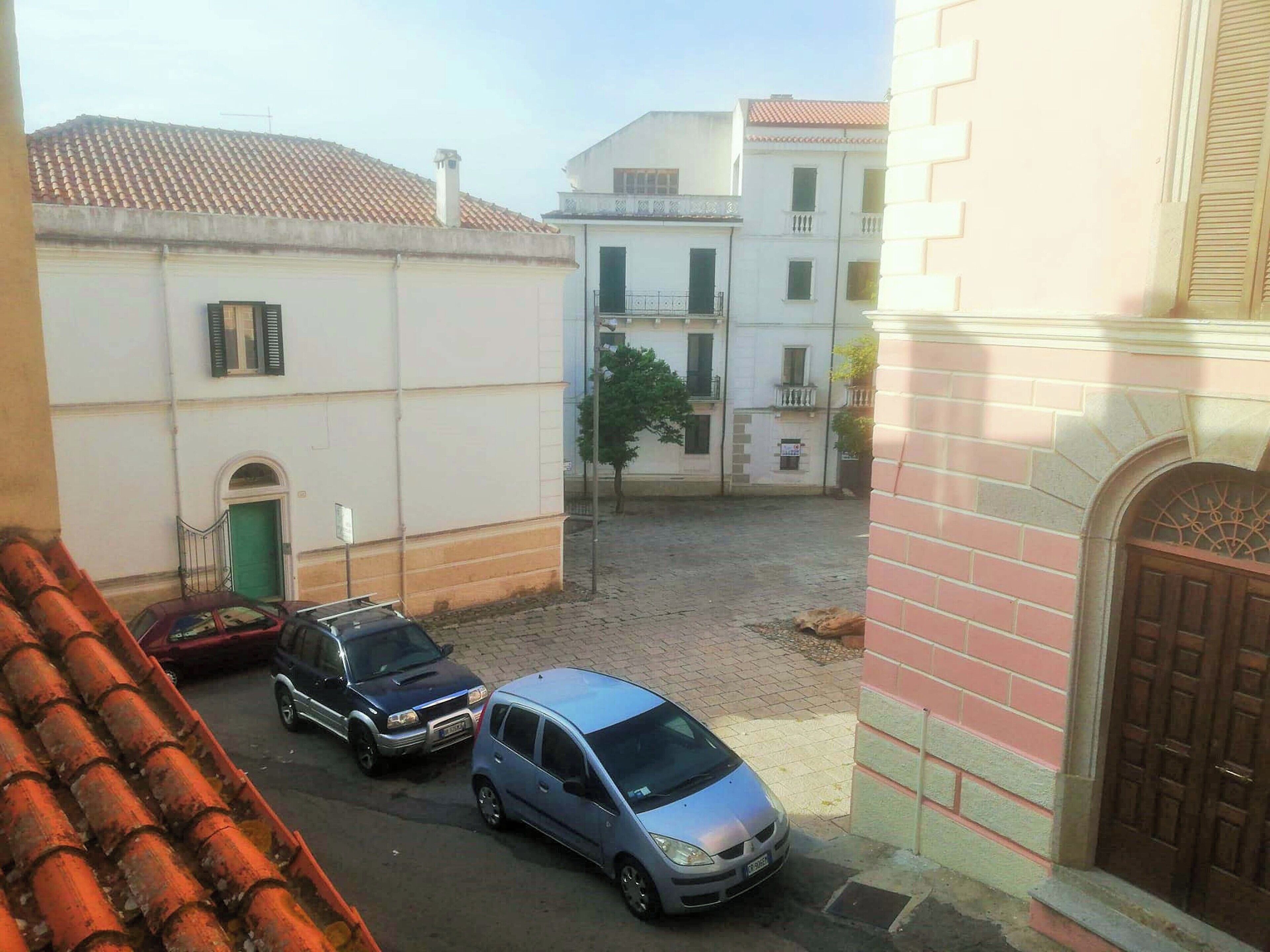 Une cour où sont garées des voitures, un bâtiment avec une porte verte et un mur de briques.