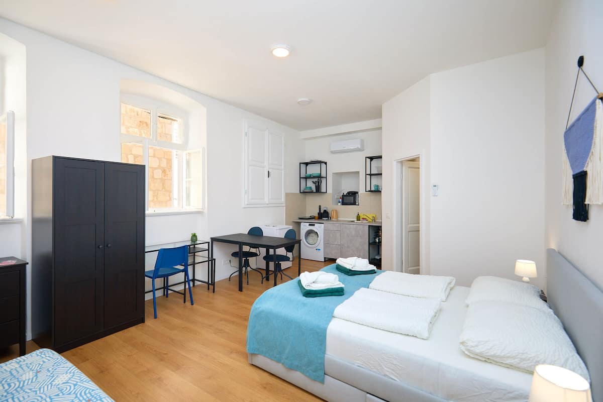 A compact room with a bed, a desk, a chair, a wardrobe, and a washing machine.