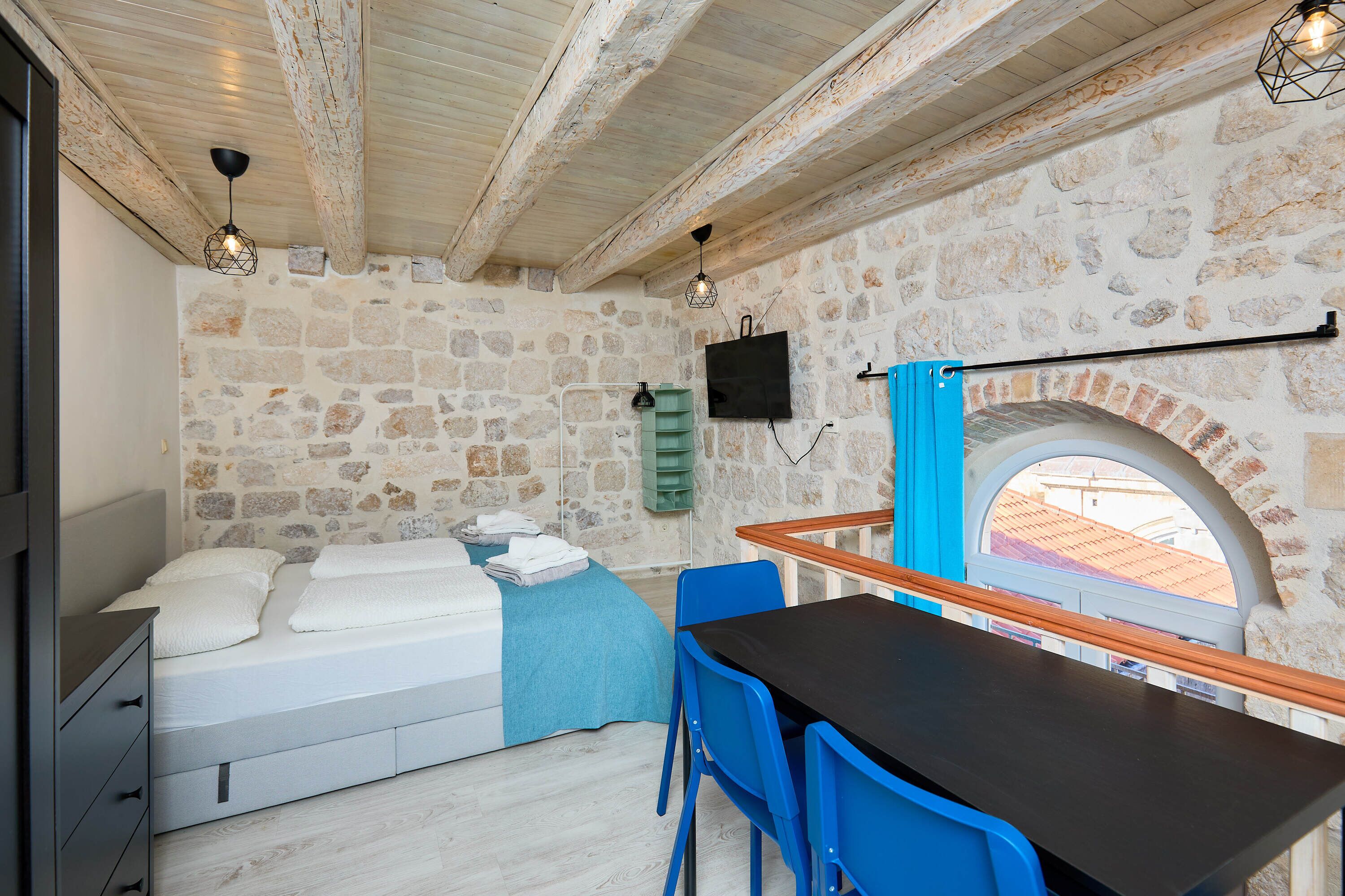 A bedroom with a bed, a desk, and a stone wall.