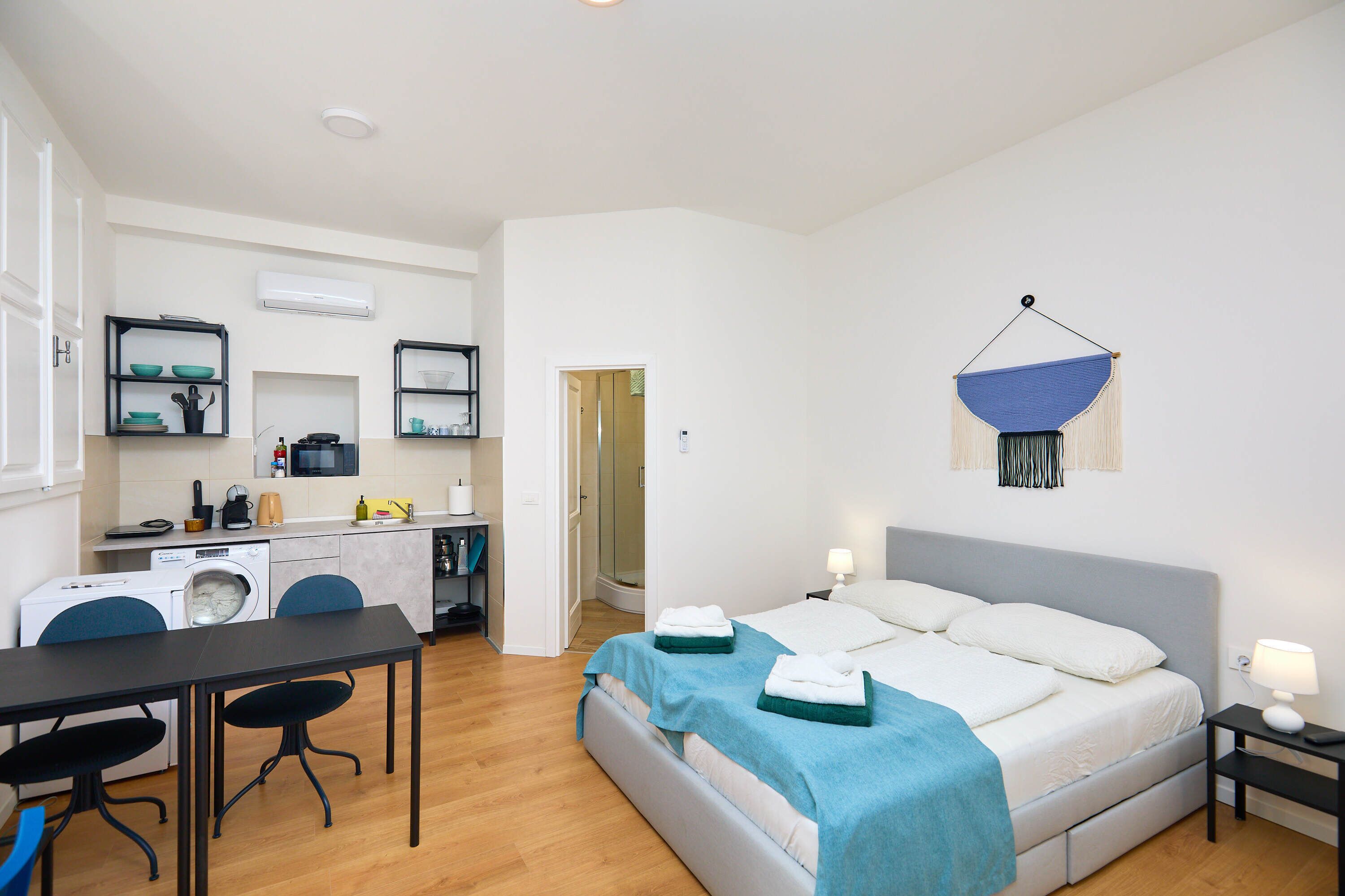 Une chambre d’hôtel compacte comprenant un lit, des tables de chevet, un bureau, un lave-linge et une kitchenette.