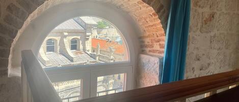 A view through a stone arch window overlooking a building with red-tiled roofs.