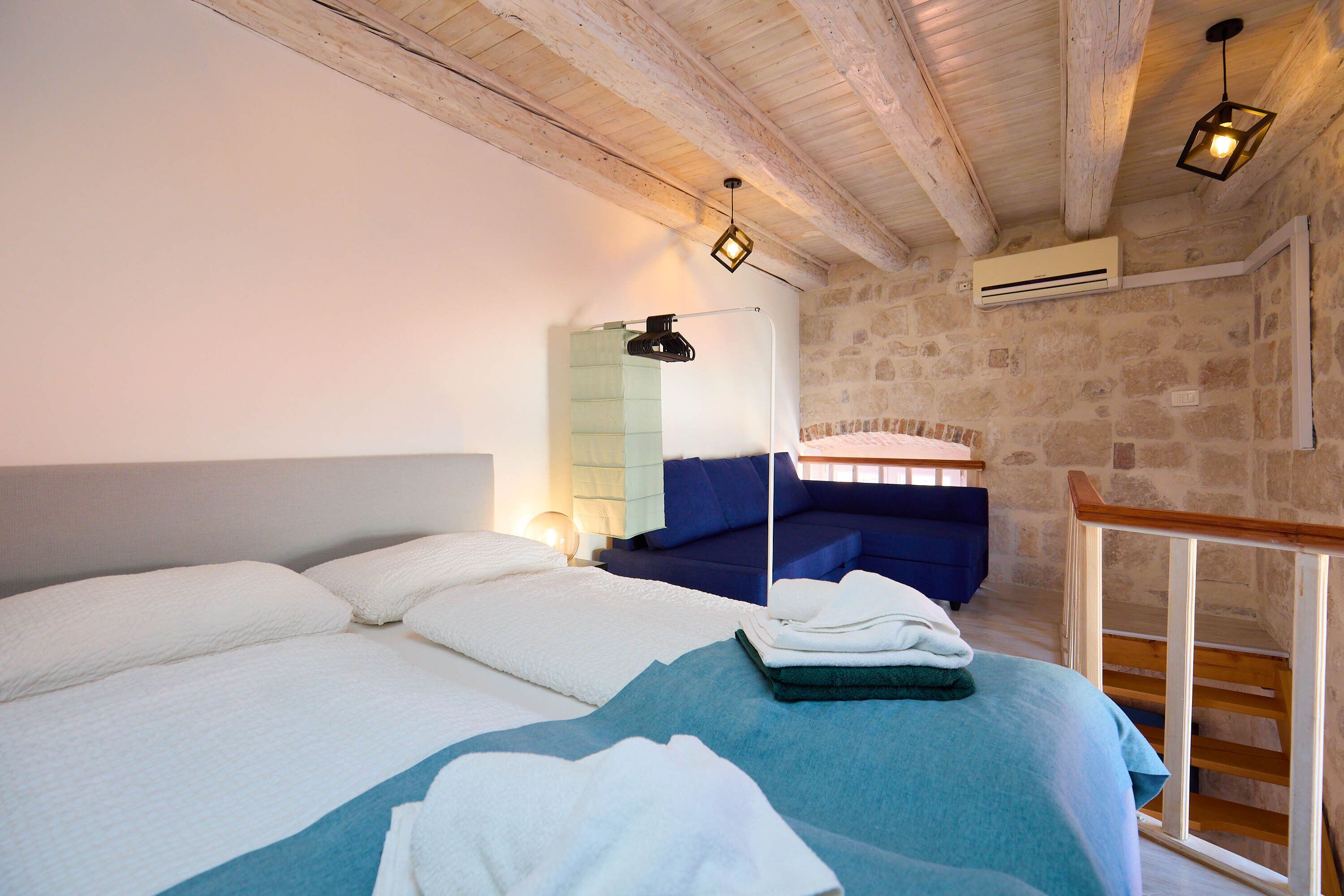 Une chambre à coucher avec un lit, un canapé bleu, un escalier en bois et des murs en pierre.