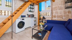 Un espacio habitable compacto con una escalera de madera, lavadora, zona de comedor y un sofá azul.