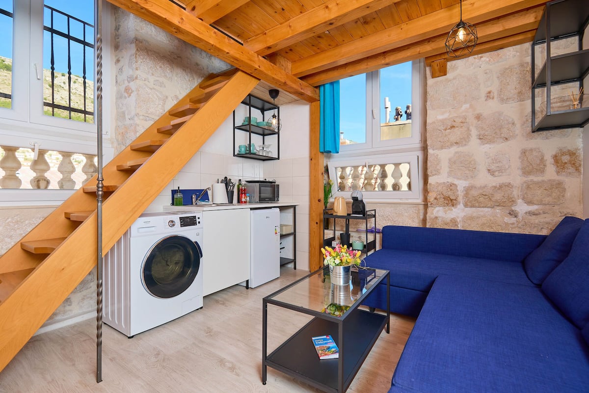 A compact living space with a wooden staircase, a washing machine, a dining area, and a blue sofa.