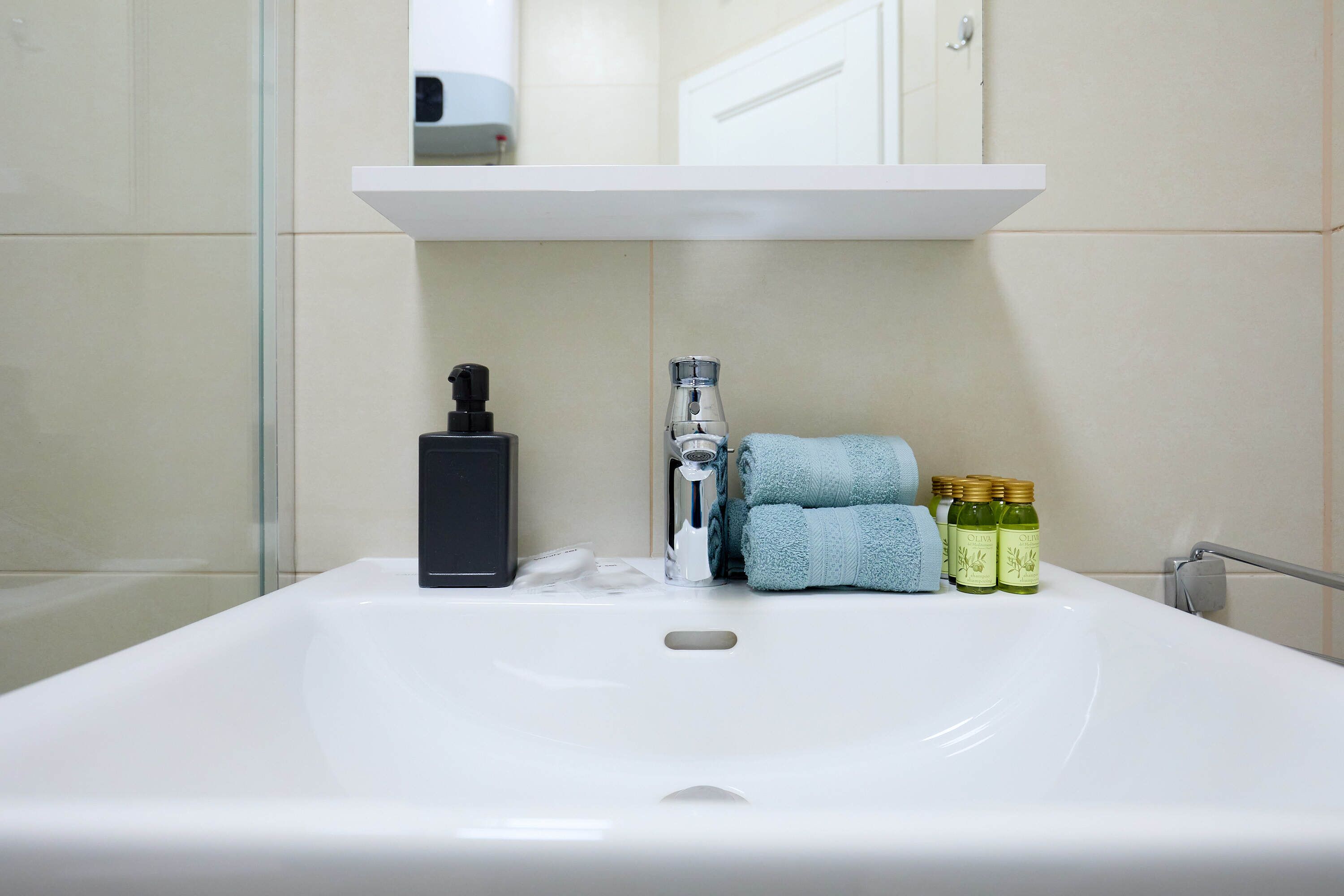 A bathroom with a white sink, a mirror, a towel, and three bottles of olive oil.
