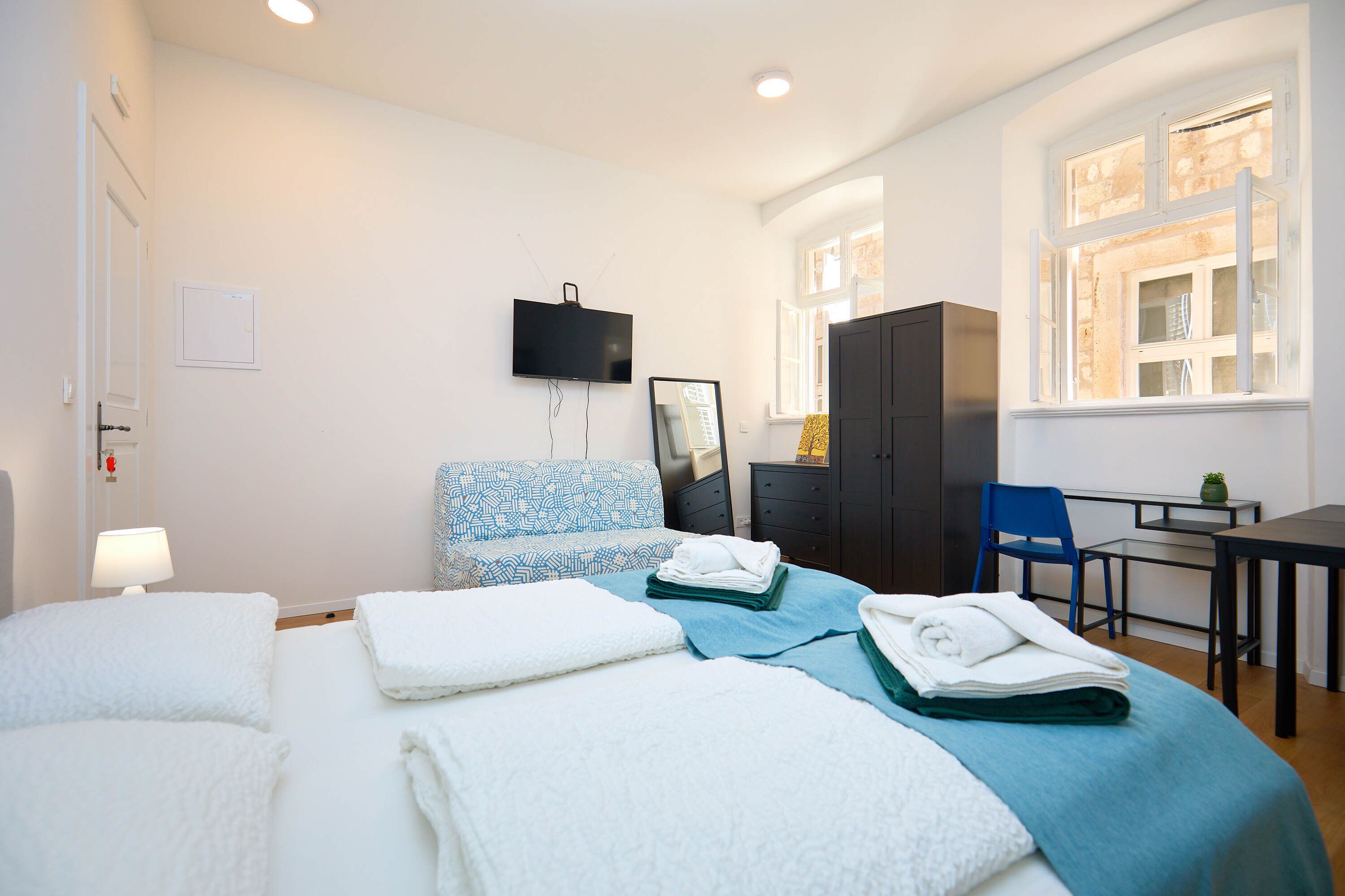 A hotel room with a bed, a desk, a chair, a TV, and a window.