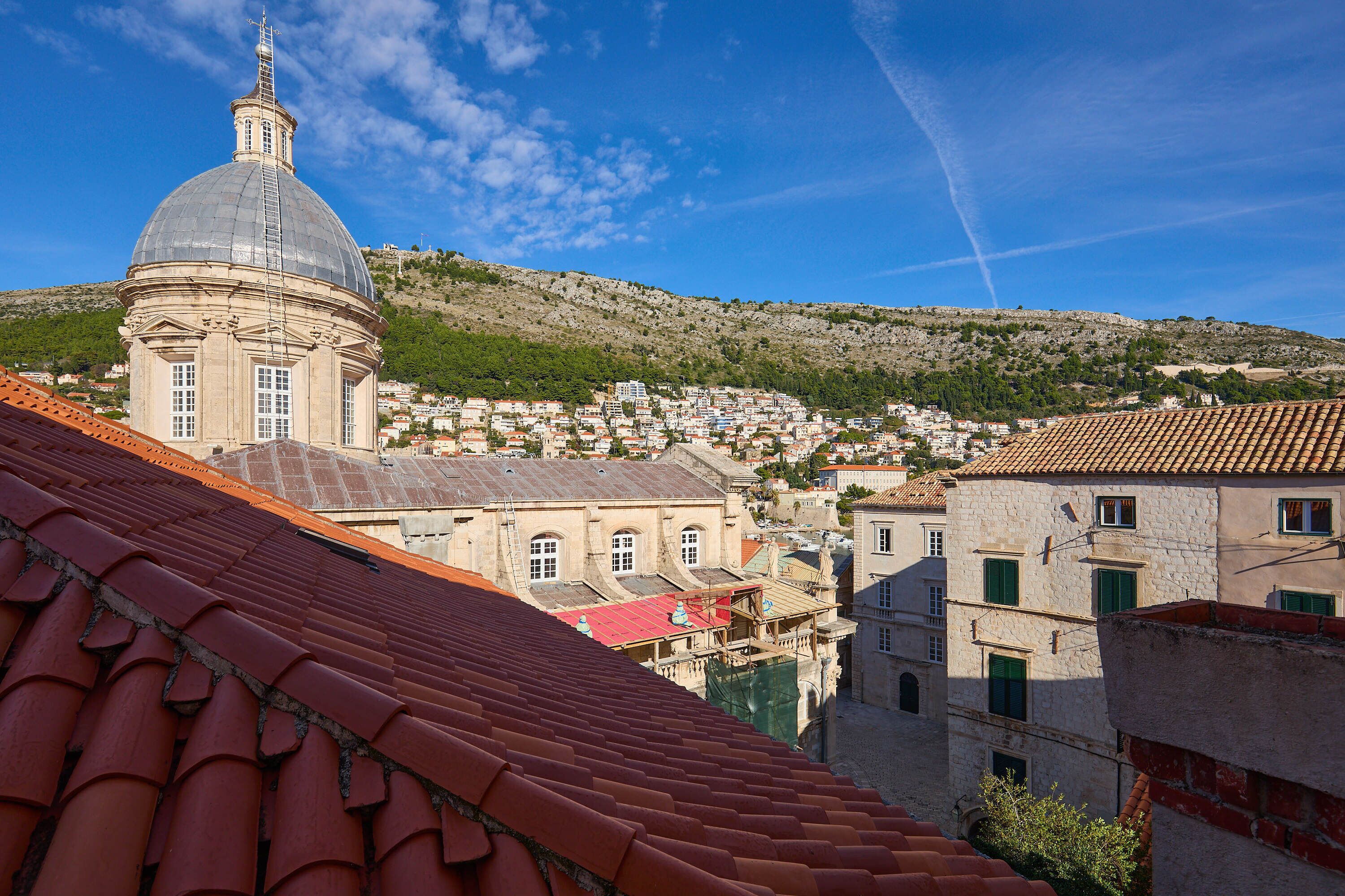 A historic building with a dome and red-tiled roofs, surrounded by a hillside town.