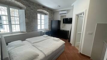 A bedroom with a large bed, a desk, a TV, and a stone wall.