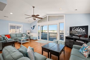A spacious living room with a large TV, comfortable seating, and a balcony with a view.