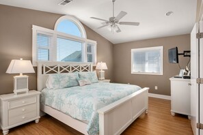 A bedroom with a bed, two bedside tables, a ceiling fan, a window with blinds, and a radiator.