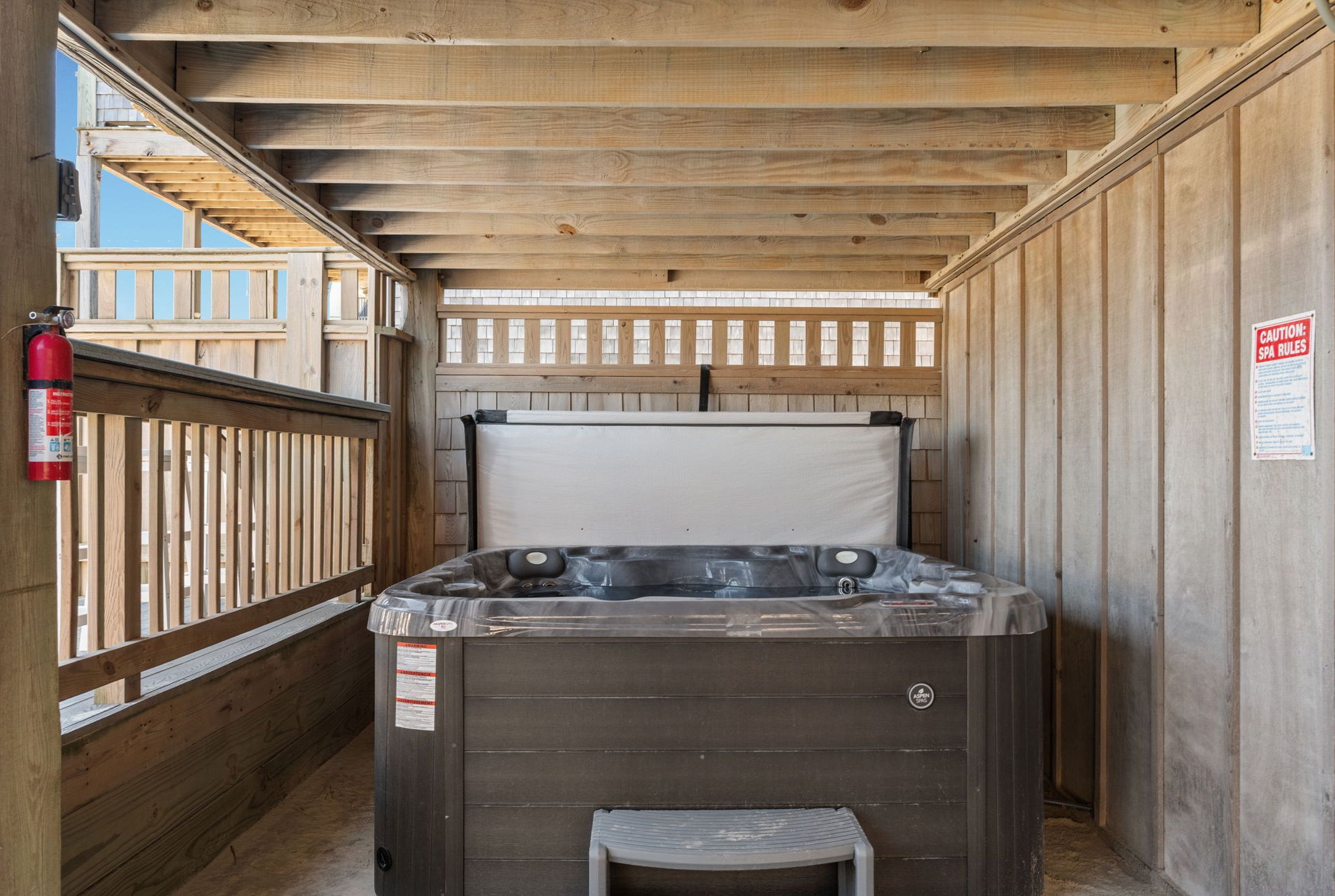 A hot tub in a wooden cabin with a wooden deck and a fire extinguisher.