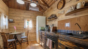 A rustic kitchen with wooden walls, a wooden dining table with chairs, a refrigerator, a sink, and a stove. - Glamping Paradise Škatlar (Novo Mesto)
