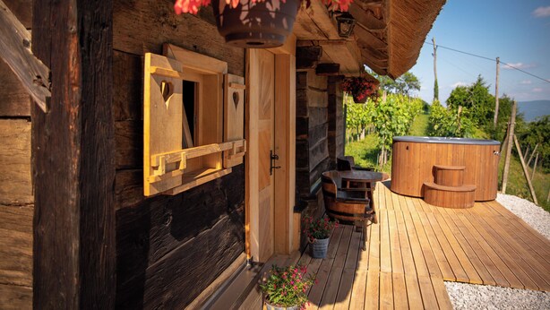 A wooden cabin with a wooden deck, a hot tub, and hanging flower baskets. - Glamping Paradise Škatlar (Novo Mesto)