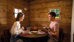 A wooden cabin interior with a round wooden table, two chairs, a pie, apples, and a radio. - Glamping Paradise Škatlar (Novo Mesto)