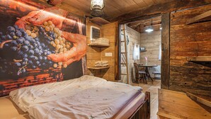 A rustic wooden room with a bed, a wall mural of grapes, a hanging lantern, and a small table with chairs. - Glamping Paradise Škatlar (Novo Mesto)