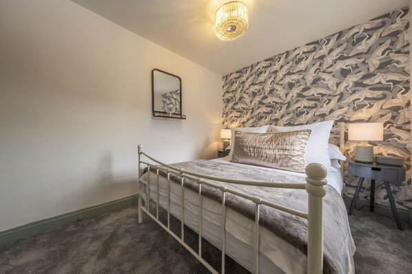 Une chambre à coucher avec un lit, une table de chevet, une lampe, un miroir et un papier peint à motifs.