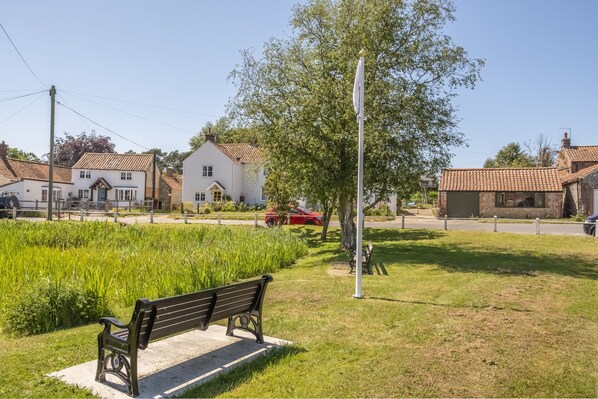 A park with a bench, a tree, and houses in the background. - The Forge (E), Edgefield, Norfolk (Edgefield)