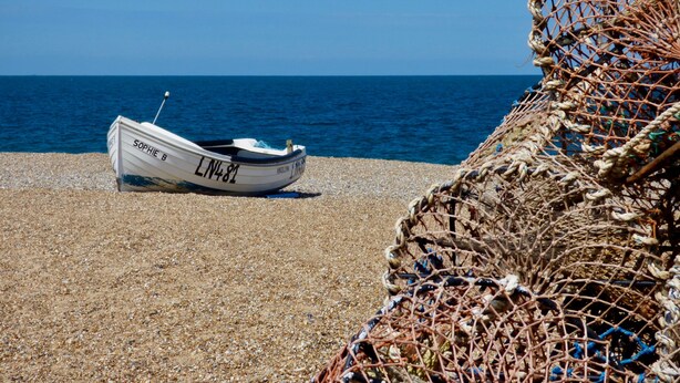 Ein Boot namens 'Sophie B' an einem Kiesstrand, im Vordergrund Fischernetze.