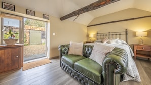 Ein Schlafzimmer mit einem grünen Ledersofa, einem Bett mit gesteppter Bettdecke und einem Holznachttisch.
