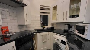 Une cuisine compacte avec des meubles blancs, un plan de travail noir, un four encastré, un four à micro-ondes et un lave-linge.