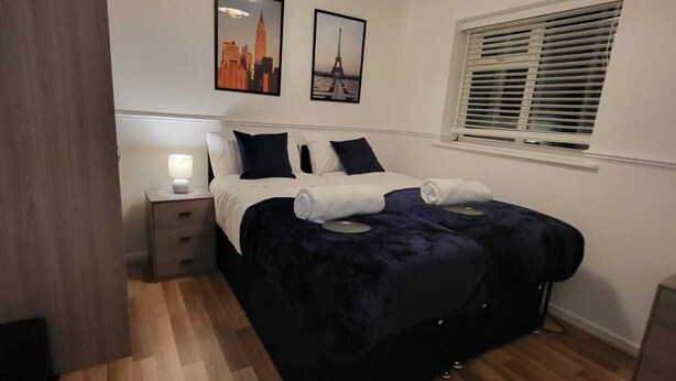 Une chambre à coucher comprenant un lit, une table de chevet, une lampe fixée au mur et deux tableaux encadrés.