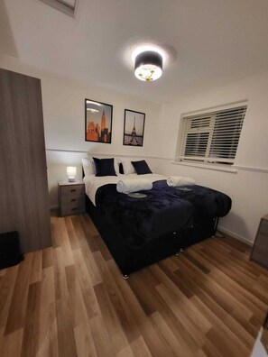 Ein Schlafzimmer mit einem Bett, einem Nachttisch, einer Wandlampe und zwei gerahmten Bildern.