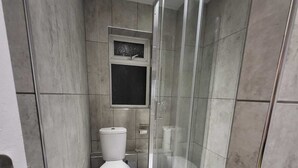 Une salle de bain moderne avec une douche à l’italienne en verre, des toilettes et une petite fenêtre située au-dessus des toilettes.