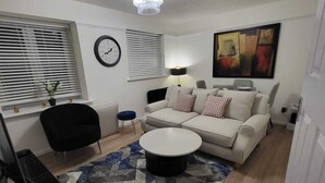 Un salon avec un canapé, une table basse, un téléviseur, une horloge et un tableau accroché au mur.