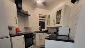 Une cuisine moderne avec des armoires blanches, un plan de travail noir, un four encastré et un ventilateur de plafond.